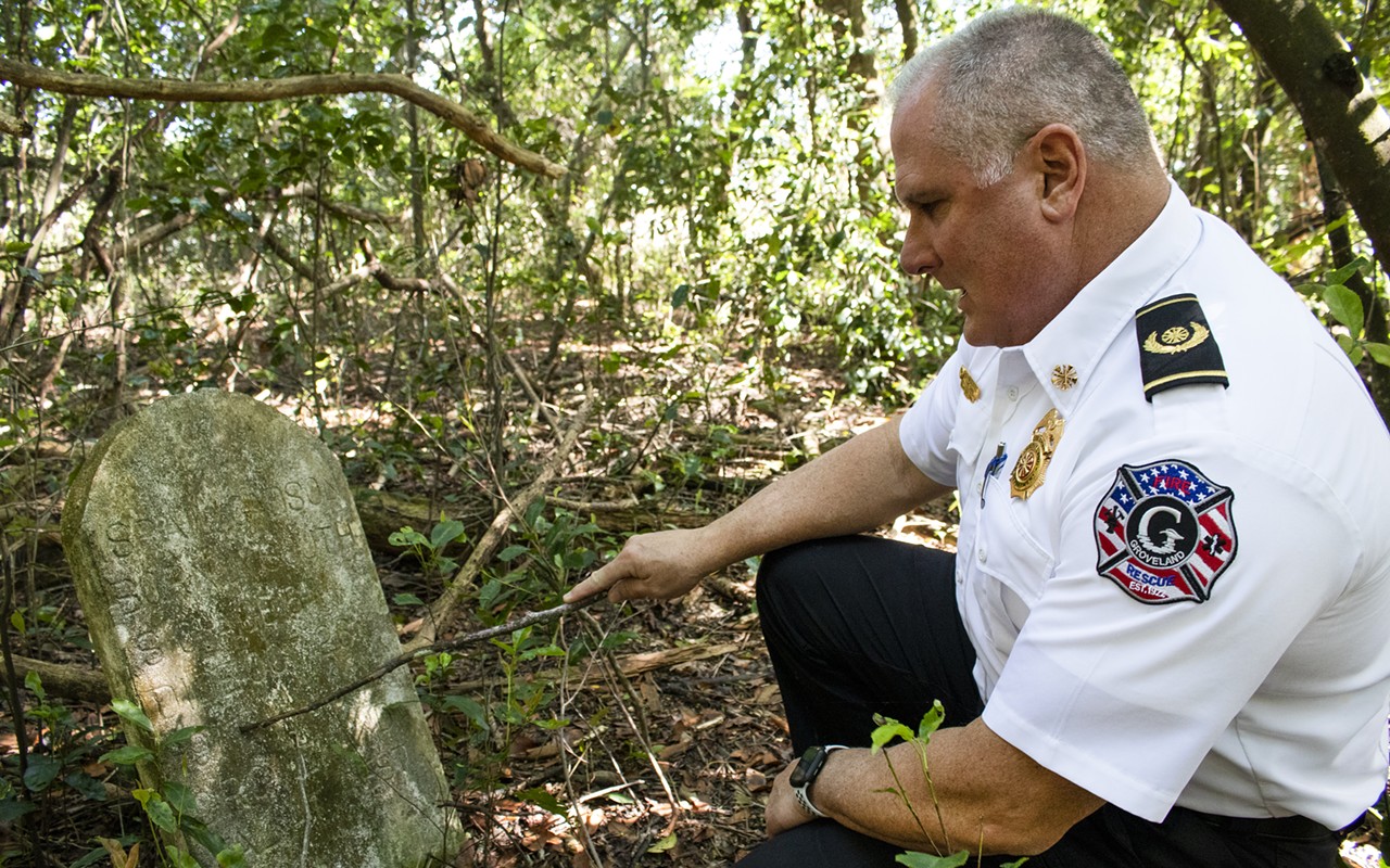 Fire Chief Kevin Carroll reads off the faded lettering on a headstone in the Oak Tree Union Colored Cemetery of Taylorville in Groveland, Fla., on Friday, March 25, 2022. The abdandoned African American cemetery is estimated to have around 70 people buried in it, according to Carroll.