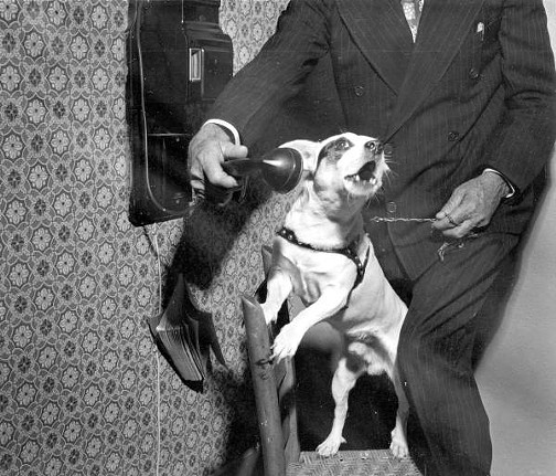 Dog barking into the telephone. Published 1957.