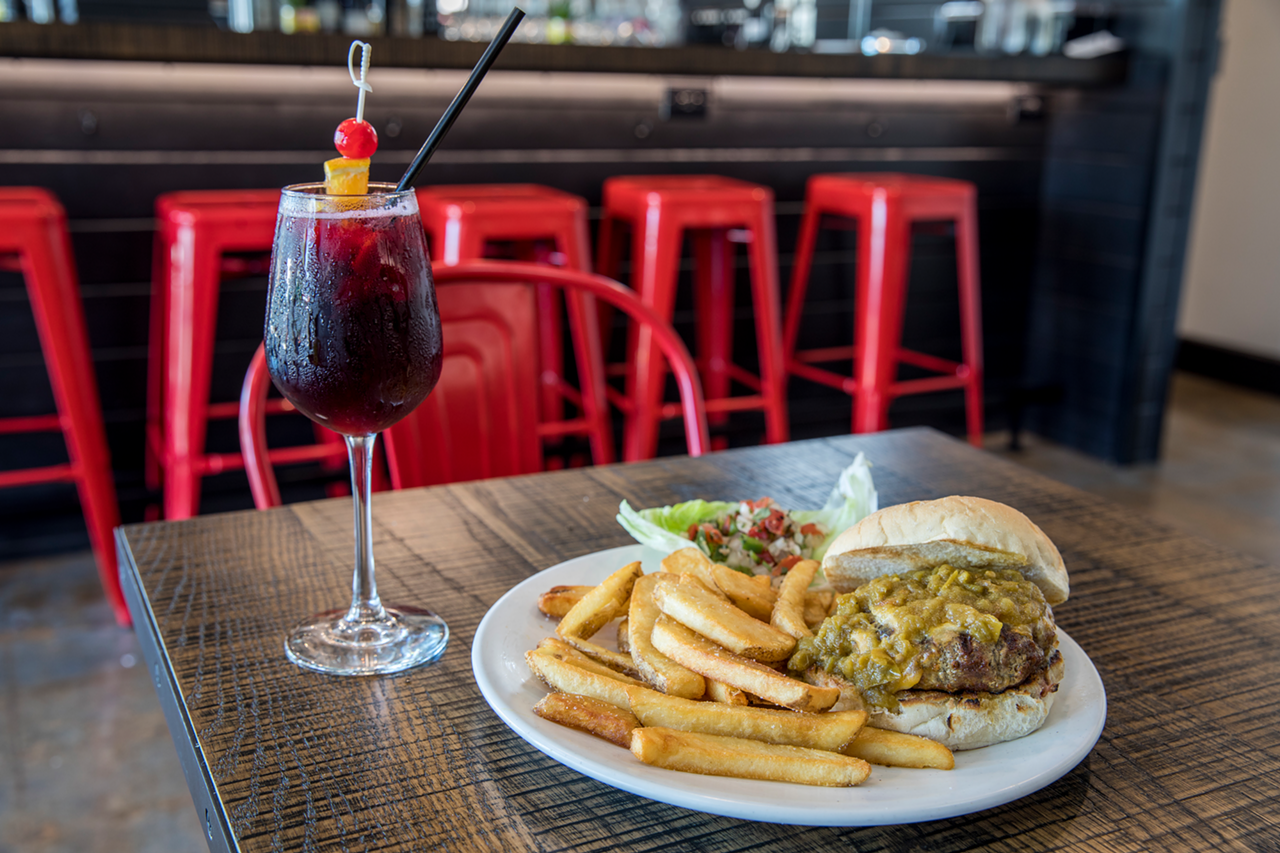 A mound of uncontrollable green chiles tops the NuMex green chile cheeseburger, accompanied by a glass of red sangria.