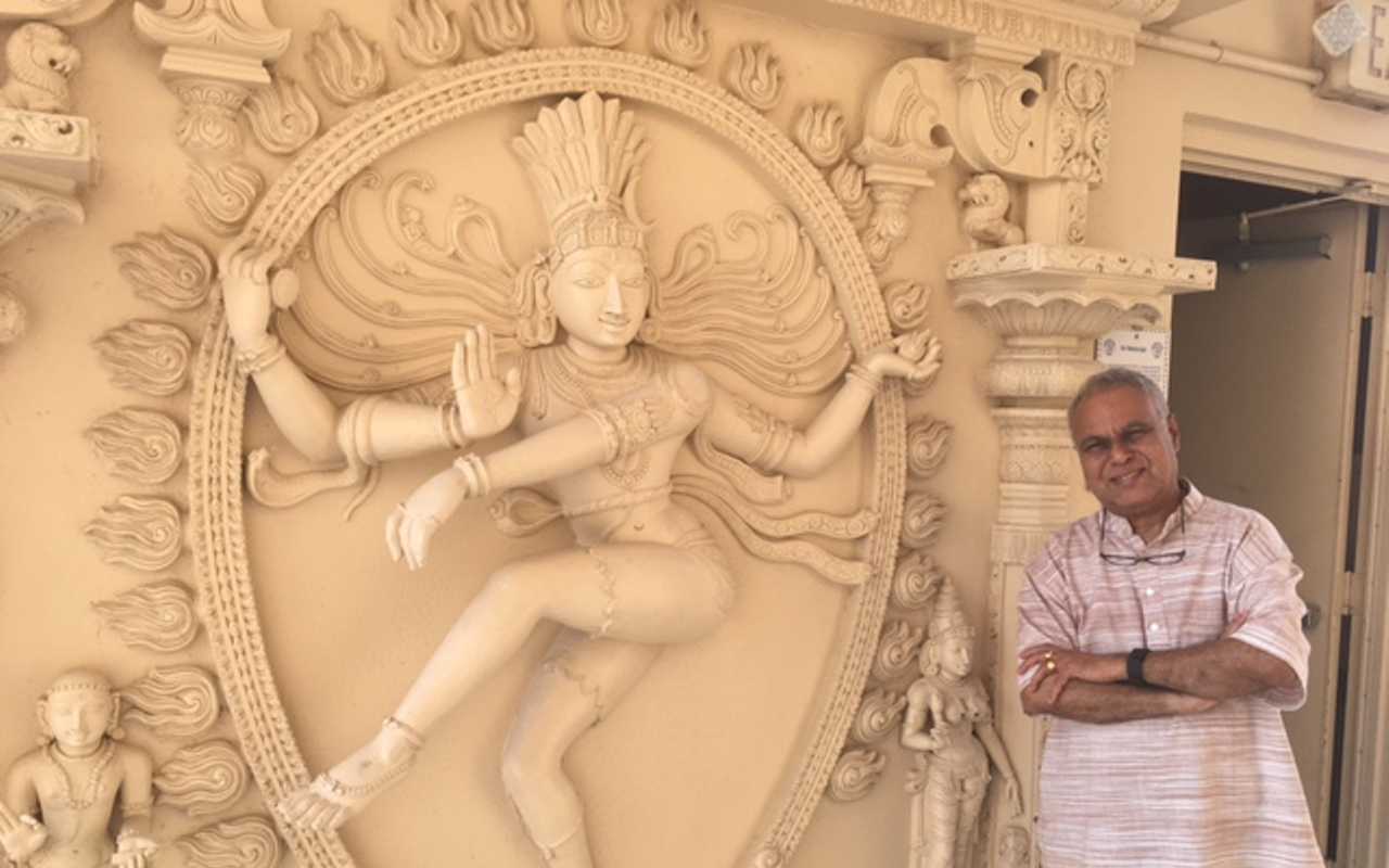 Temple guide Dr. Sridhara Sastry stands near a depiction of the major Hindu god Shiva, the Lord of the Dance.
