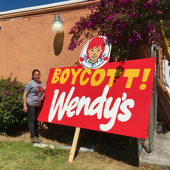 CIW's Nely Rodriguez stands outside the CIW headquarters with a sign the group uses to raise awareness for workers' plight. - Cat Modlin-Jackson