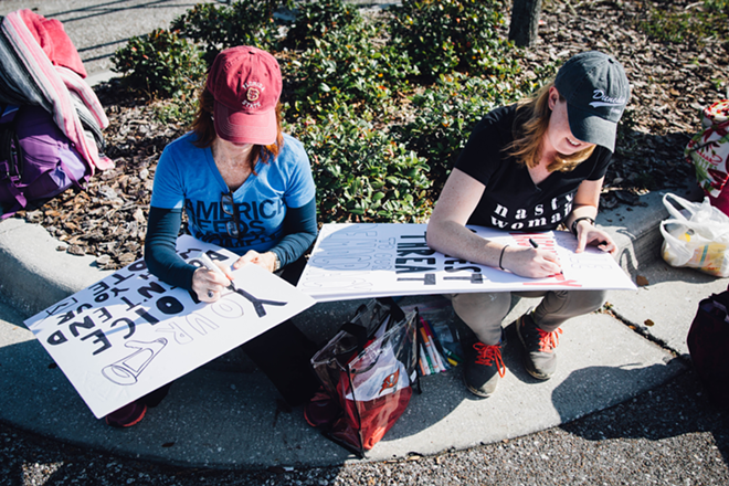 Two young women create protest signs as they wait. - Anthony Martino