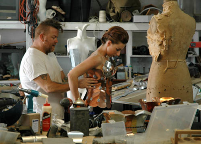 RIVETING: Strunk helps his model, Lindsay Dobrowolski, into a copper corset at his Gulfport studio. - CARRIE WAITE/HAIR AND MAKE-UP CAREY HINRICHS
