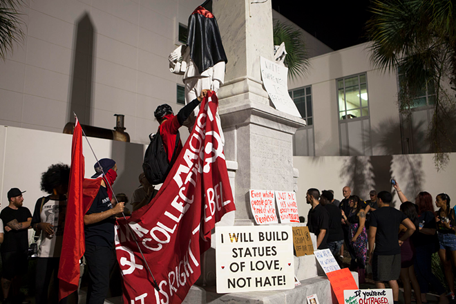 During a Sunday night march against neo-Nazis and the KKK, activists place anti-hate signs and banners on the controversial Confederate monument in downtown Tampa. - Kimberly DeFalco