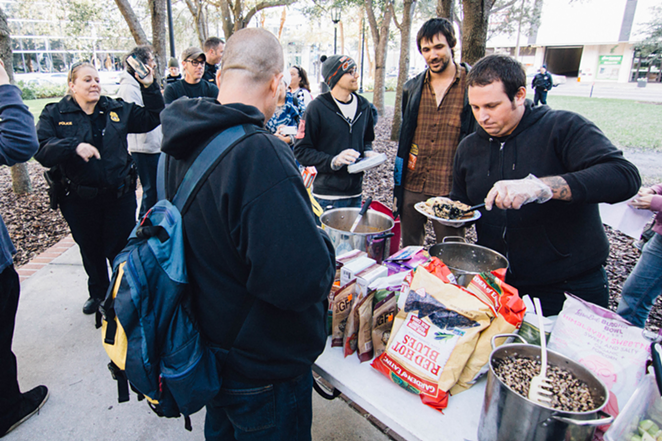 A volunteer serves food as police linger nearby. - Anthony Martino